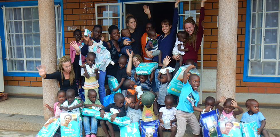 Kinder und Betreuerinnen im Freiwilligeneinsatz vor der Schulpforte des Babies Home in Kampala, Uganda.